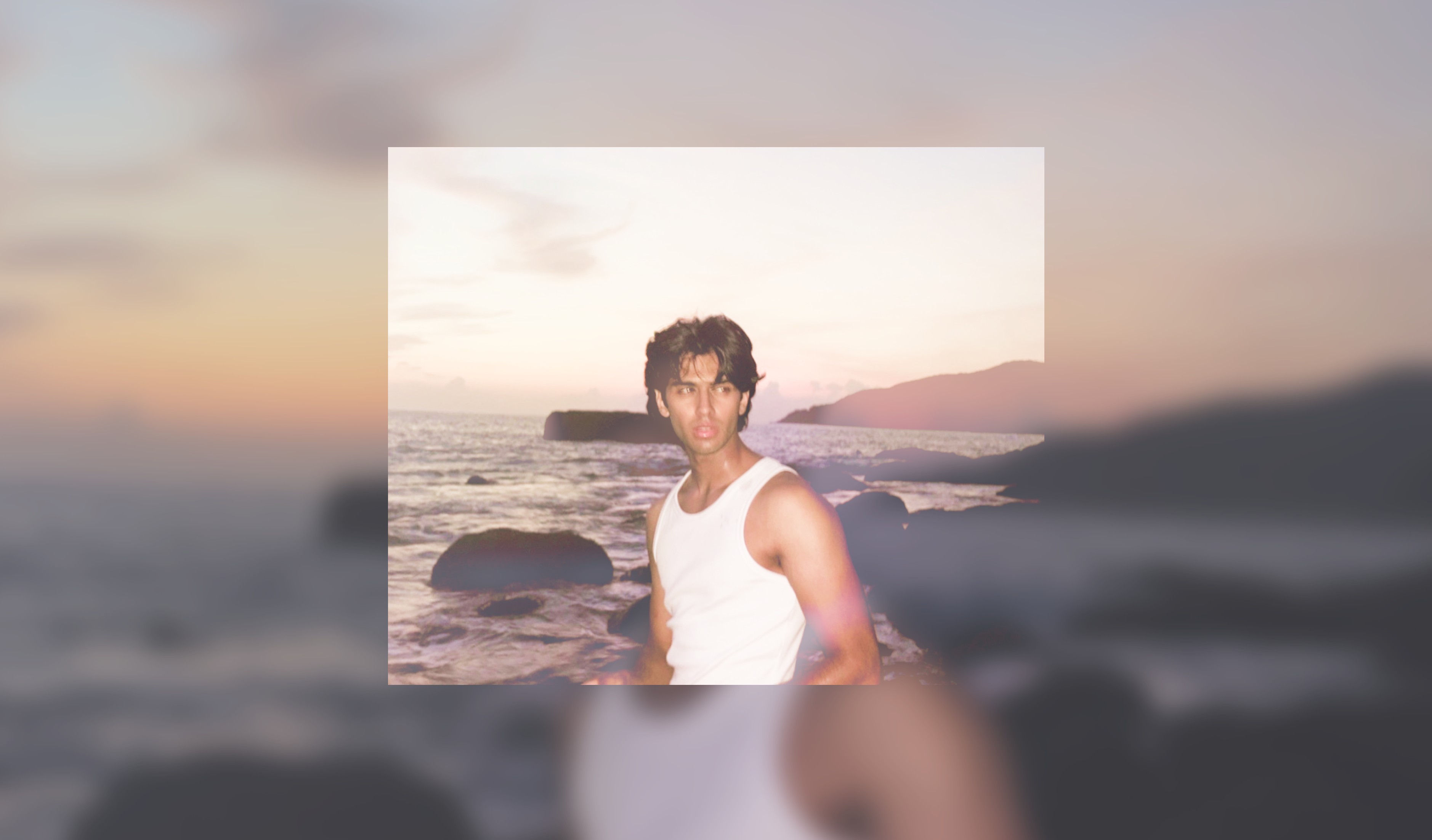 Kunsh on a rocky beach at dusk, in a white vest.